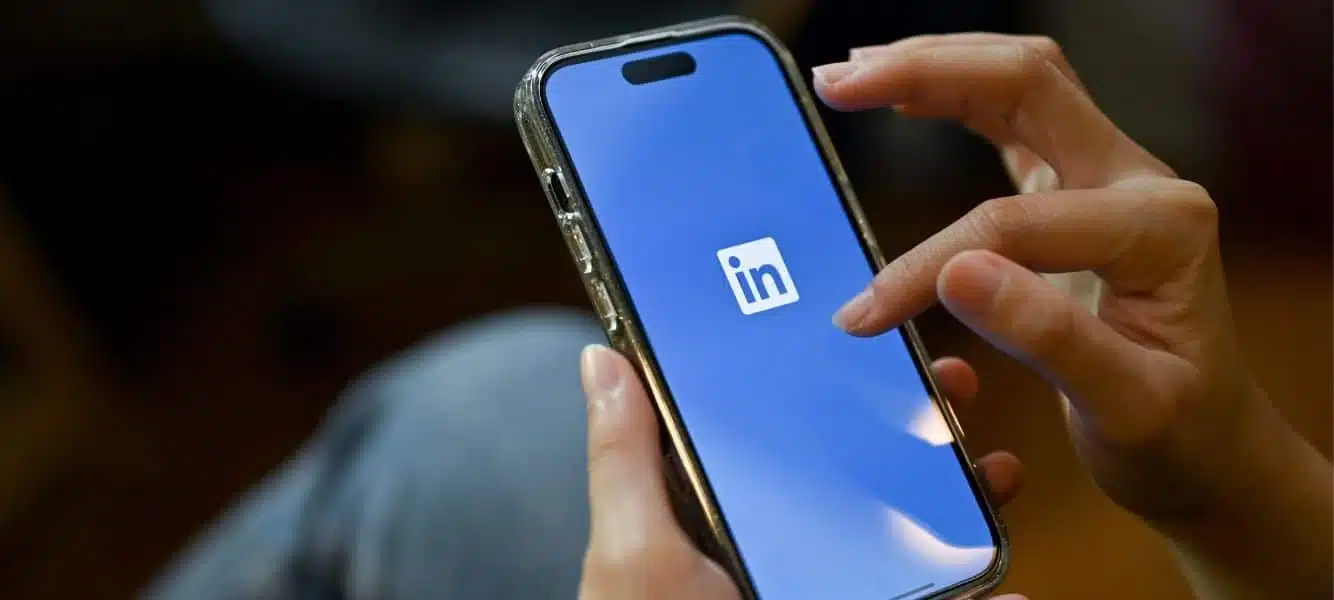 an image of a person on a mobile phone, they are using the LinkedIn app - this is the featured image on a blog entitled improving your linkedin profile