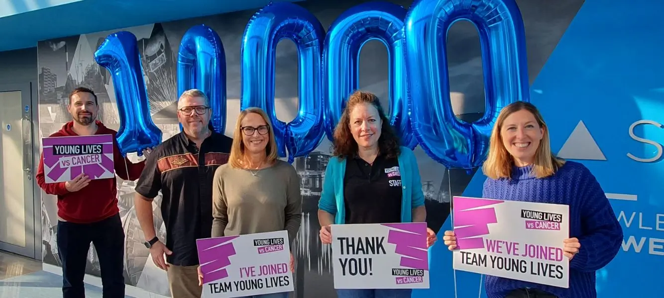 An image of four of energy recruitment agency Astute's team holding Young Lives vs Cancer signs, they are stood in front of balloons in the shape of the number 10000