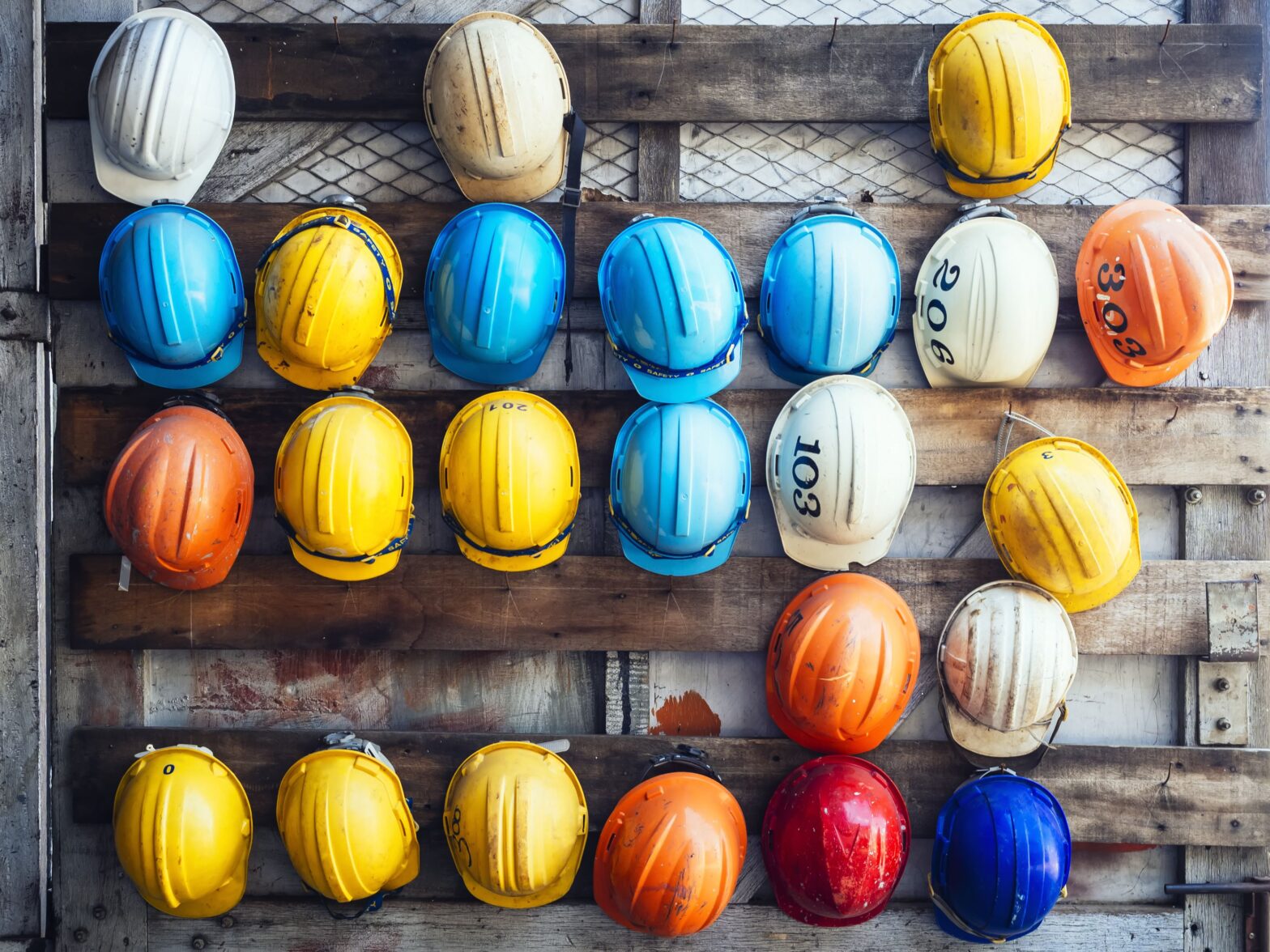 A wall with 25 construction helmets in many different colours. They are yellow, blue, white, orange, red, dark and light blue. Symbolise the New APSCo Labour Data.